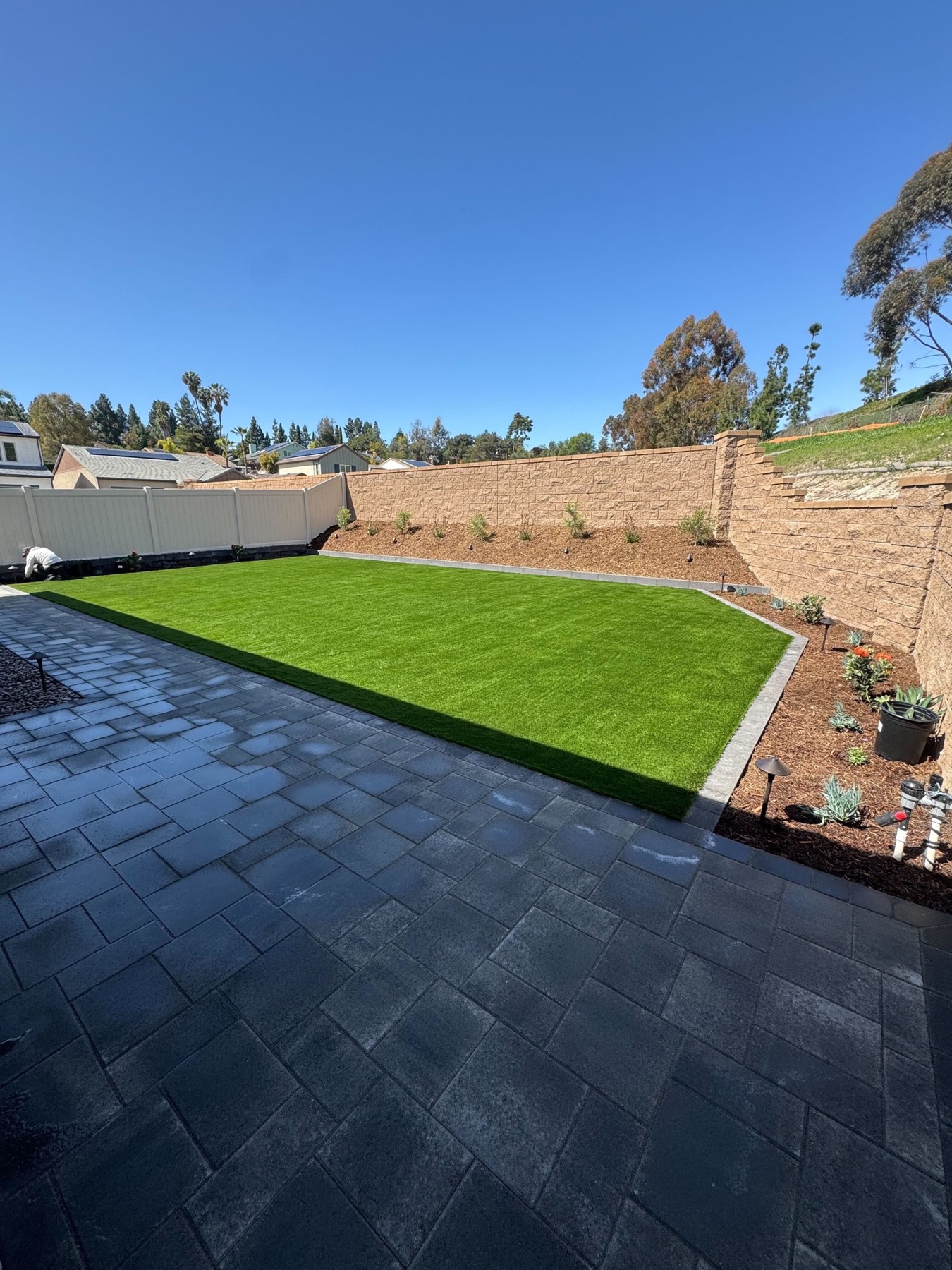 Backyard remodel with a charcoal paver patio, artificial turf lawn and retaining wall by Abshire Brothers Lawn & Landscape Rayne